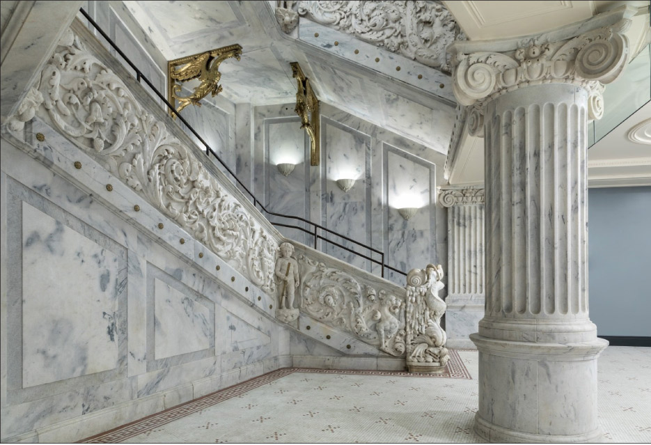 A watchful winged lion stands guard at the base of the opulent marble-clad grand staircase.