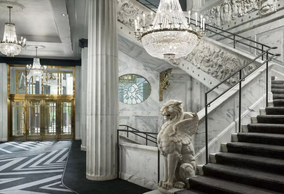 A watchful winged lion stands guard at the base of the opulent marble-clad grand staircase.