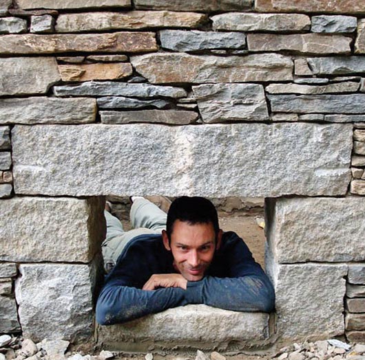 Archambault takes a quick rest in the opening for a natural stone pig roaster after working