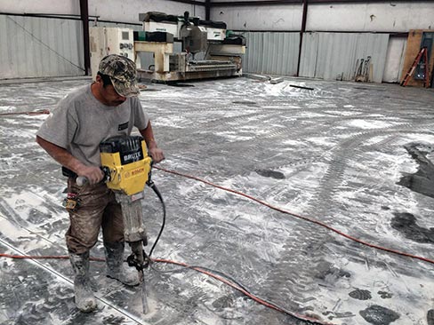 After lines have been carefully cut in the concrete with a concrete saw,  a jackhammer is used to lift out the flooring so that trenches can be cleanly dig with larger machinery.