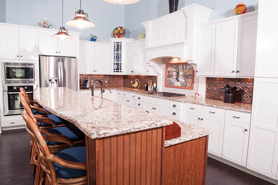 A breakfast bar and prep area sit across from a magnificent array of Aristokraft Winstead Maple White cabinets. The 3cm Santana granite countertop, with stove bump-out, flows end to end, adding a touch of elegance to this light-filled residence. 