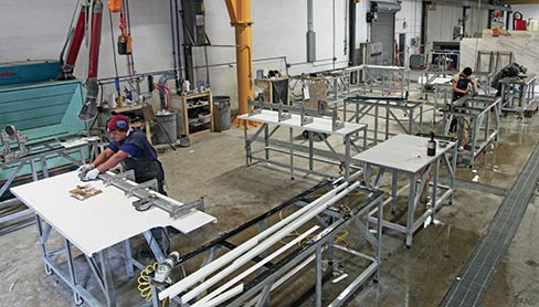 At left, eight-year veteran CCS Stone fabricator Yony Jolon glues a mitered countertop, while two-year fabricator Mario Rivas polishes the backsplashes. Also hard at work is six-year fabricator Leo Moreno polishing  a sink hole in a Green Rose Granite countertop. Covering these handwork stations is a Farnese 500 kg, 21 foot jib crane that utilizes an Abaco clamp lifter and Abaco vacuum lifter. The well-designed shop features a dust collection machine with articulated arms that can pull in 8,000 cubic feet of air per minute, and  an electric water heater used to warm the water being fed into the hand polishing tools–especially welcome during the winter months. 