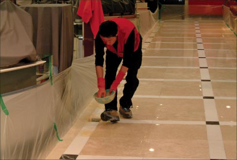 Applying Stone Polishing Compound on a large retail space, preparatory to using an auto-scrubber. Note the taped-off and drop cloth-protected areas. 