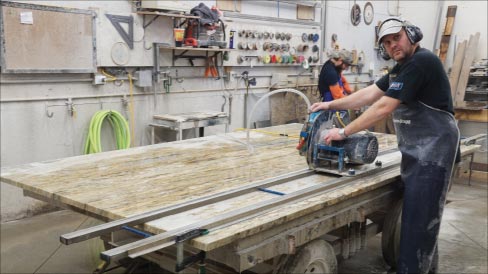 Matt Hoffmeyer’s cousin, Terry (foreground), says the company’s Blue Ripper rail saw has been a workhorse for them, very efficient and easy to use. In the background, Matt’s son Harrison Hoffmeyer wet polishes that week’s kitchen. The Blue Ripper came from Braxton-Bragg, as do many of their production tools and supplies. 