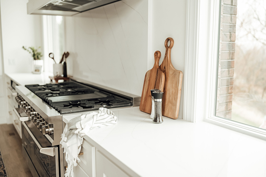 Custom quartz kitchen includes a large central island for prep and dining, and a full-height splash behind the commercial grade range.