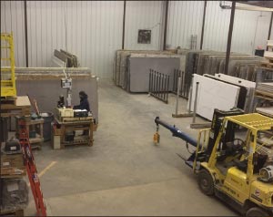 Solid Surface Designs’ old slab storage system made for less free space to extract slabs from a rack, and increased forklift travel. They use a slab photo scanning and bar code system to track slab inventory, work station seen at center left.