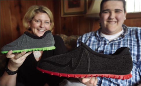 Broc Brown, right, shows off his new shoes with Feetz CEO Lucy Beard at his grandmother’s home in Michigan Center, Michigan. Brown, who has Sotos Syndrome and is 7 feet, 6 inches tall, was given a new pair of size-28+ shoes from Feetz. Feetz uses an app to convert photos of someone’s feet to a 3-D model, to build custom-sized shoes using 3-D print technology.