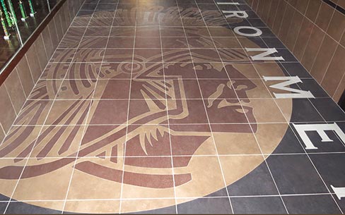 Custom logo art can be created in most hard surfaces to match the surrounding flooring, or in the case of middle and high school emblems, to meet a range of school budgets. The more colorful renditions can incorporate a variety of durable, hard materials including stone, tile, metal, glass, concrete or terrazzo.