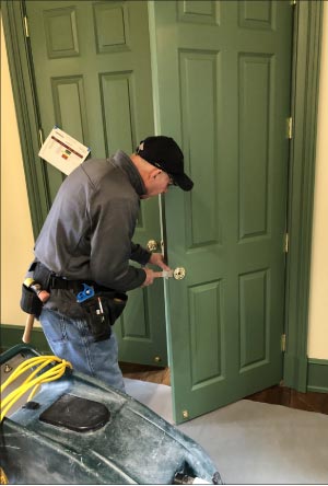 A hardware specialist installs custom fittings on these oversized doors. Note the protective drop cloth laid down to protect the new hardwood floors. Sharing construction space and cooperating with other contractors is a challenge when your area of concern is the floors, and either restoring them or preventing construction damage like stains and scratches.