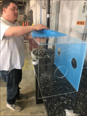 Stone Studios employee Justin Moore finishes an aerosol protection box to be used by health care providers when intubating COVID-19 patients. The company’s main business is selling granite, marble and quartz countertops, but it recently began using its fabrication equipment to build the boxes, which protect clinicians, nurses and doctors from contamination.