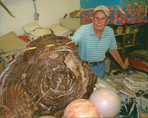 Bryant Washburn stands in his garage behind a petrified wood slab that hails out of Southern Utah. He has more than 10,000 pieces in his collection