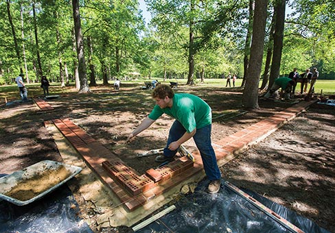 A double-wide course of pavers were used for strength as well as to assist viewers’ comprehension of the overall size of the home. Six courses double-wide were then laid using large brick at all four corners and then capped with pavers. Masonry construction will resume this fall by the next freshman class.