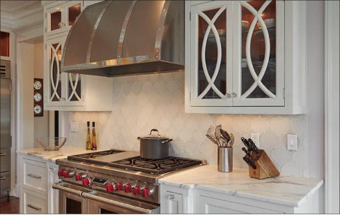 This custom marble kitchen includes matching, hourglass-shaped mosaic marble backsplash tiles.