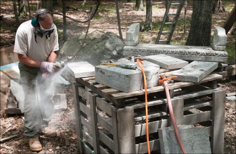 Michael Jamieson is in the middle of beveling and bush hammering newly fabricated stone components to match the antique bench shown in the background. He then carved hand and foot prints of his client’s children into the surface of the seat. Most of Mike’s work is done with smaller air and electric hand tools.