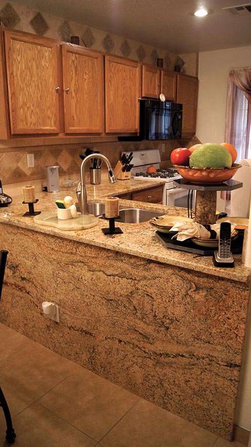 Kitchen counters and coordinating cladding from a honey-colored slab of Giallo Antigua. Backsplash is coordinated Ivory and Noche travertine. Note the matching cake stand made from a column of Giallo with Black Granite base and top.