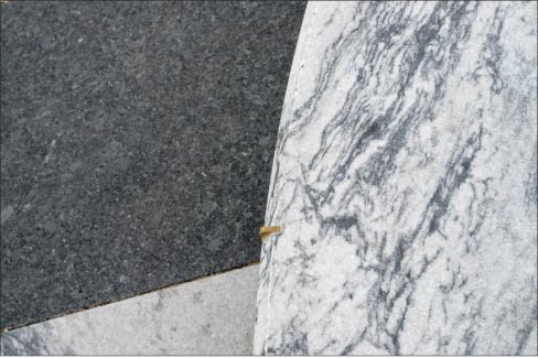 A detail perspective of a carved round Pearl Grey marble bench shows the contrast with a Laurentian Green granite paver.