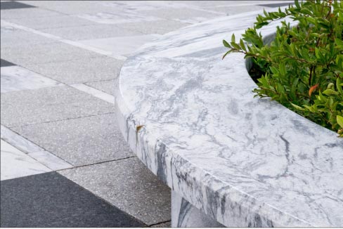 A detail perspective of a carved round Pearl Grey marble bench shows the contrast with a Laurentian Green granite paver.