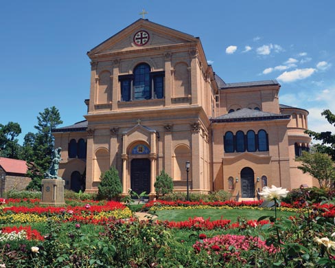 The Monastery is pictured from outside with a lawn of flowers leading in.