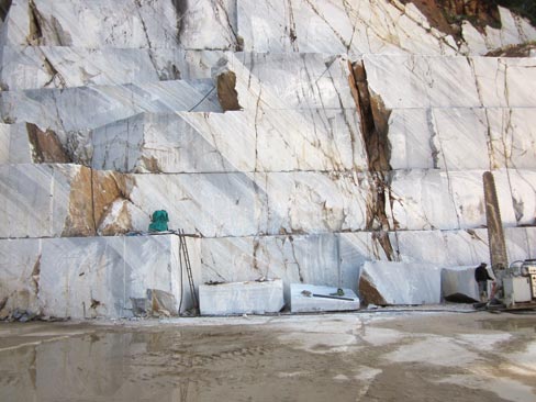 At far right, a diamond wire saw arm stands poised and ready for its next cut as the benches of blocks are dropped in this Cremo Delicato marble quarry in Carrara. 