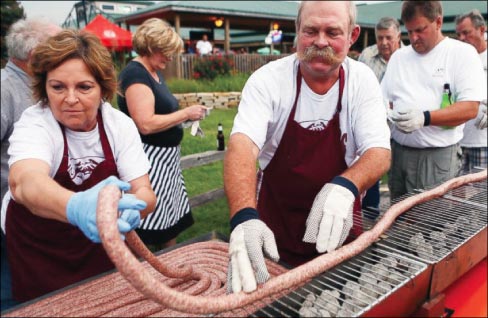 In this Sept. 9, 2014 photo, Mabel and Larry Schubert help lay out a 100 foot-long bratwurst on a grill at the Silver Creek Saloon in Belleville, Ill. About 50 people volunteered to carefully grill the bratwurst without burning or breaking it. The event was a practice run for the Belleville 200th celebration where they grilled a 200 foot-long bratwurst.  Photo: Zia Nizami, AP