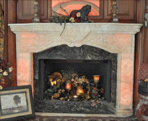 This one-of-a-kind Onyx fireplace mantel and surround were designed by artist and interior designer Cheryl Cobb. From designer’s concept, passed to Lawrence Deyoung of Stone Spectrum who did the CAD drawings, to fabrication, and to install – this was a 1 year project. The mantle and top cross piece was carved from one block of Pakistani Onyx. The legs are also of matching Pakistani Onyx. The interior frame is Black Thunder granite, obtained from Brazil. The fireplace surround is back lit with color changing LED lights, accessed by a remote control. Josh Spencer noted that the carving on the fireplace was designed to match hand-carved custom cabinetry in  the residence.