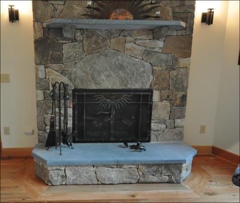 Two fieldstone fireplaces share a common wall, and tie the outside fieldstone and soapstone to the stone chosen for the interior. A similar soapstone floor to the porch fireplace room is also planned for the front porch area.