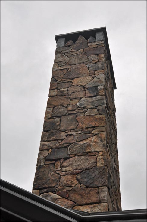 The mixed fieldstone and soapstone chimney has a beveled soapstone cap. 