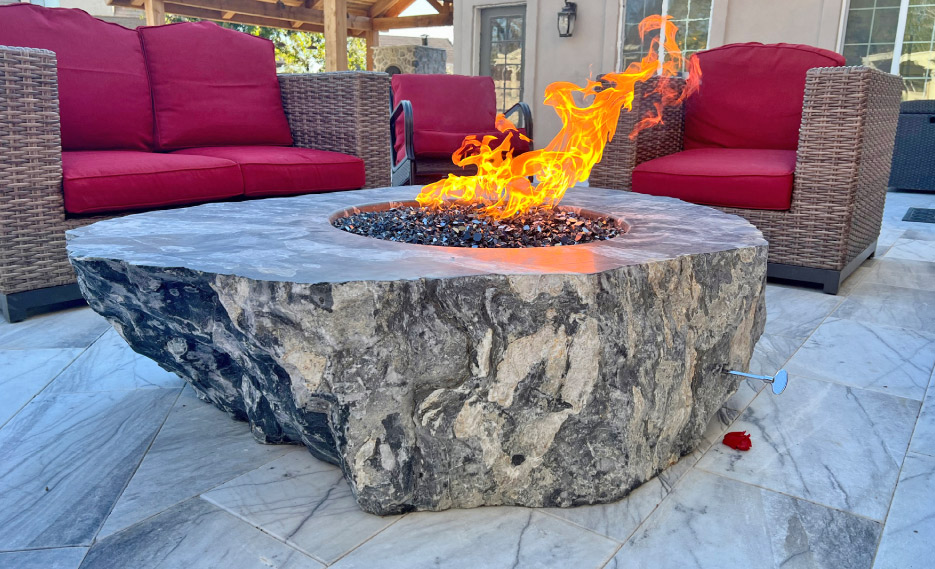 A Fire pit fashioned from an American Caviar boulder rests on Geronimo marble flagstones. 